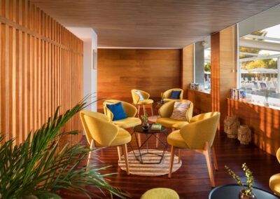 Bright lounge area with yellow armchairs, wooden elements and a view of the terrace of a modern hotel