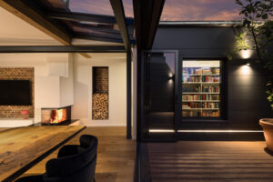 Modern architectural photography of a loft at dusk - interior with fireplace, wall of books and terrace in Hamburg