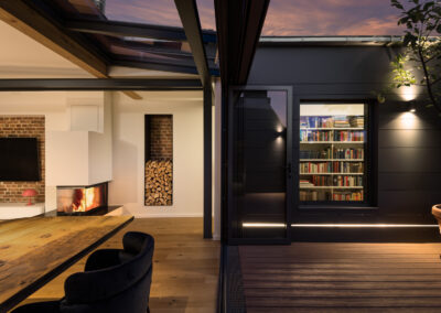 Moderne Architekturfotografie eines Lofts bei Dämmerung – Innenraum mit Kamin, Bücherwand und Terrasse in Hamburg