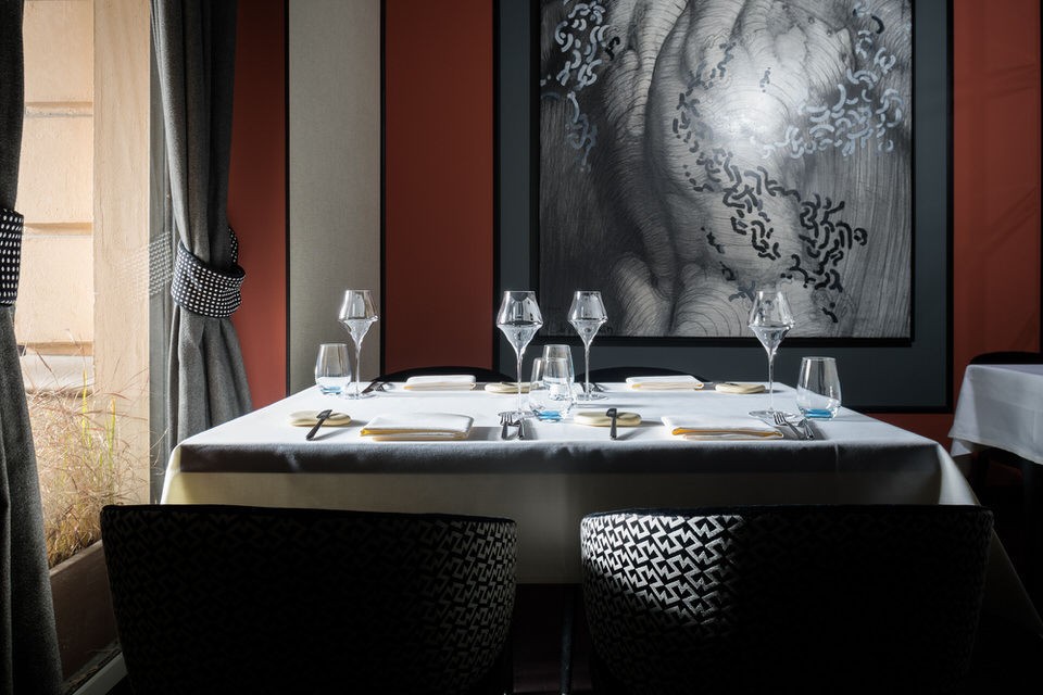 Gedeckter Esstisch neben einem Fenster durch das die Sonne scheint. Die Einrichtung ist modern, schlicht und edel mit einem modernen Wandbild im Hintergrund