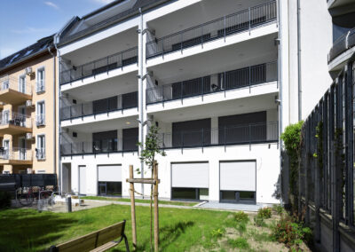 Fassade eines Neubaus mit Gartenanlage und Sitzbank im Hinterhof