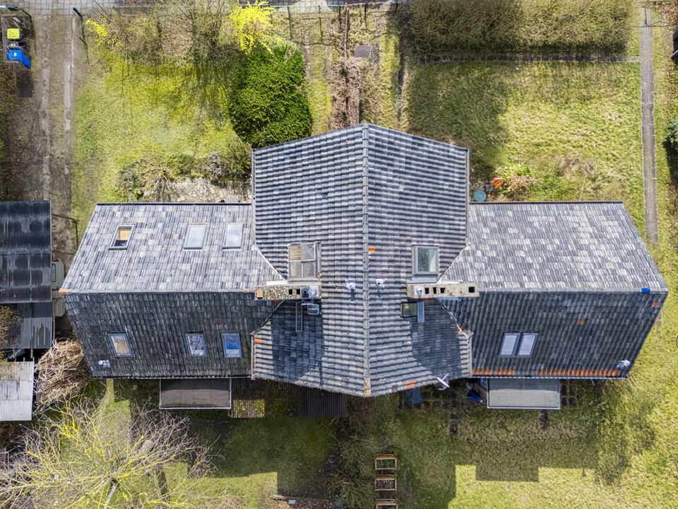 Aerial view of a residential building with a pitched roof and several skylights in the middle of a garden