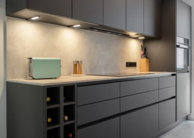 Professionelle Immobilienfotografie einer modernen, grifflosen Einbauküche in Mattschwarz mit integriertem Weinregal und LED-Unterbauleuchten in einer Berliner Wohnung.